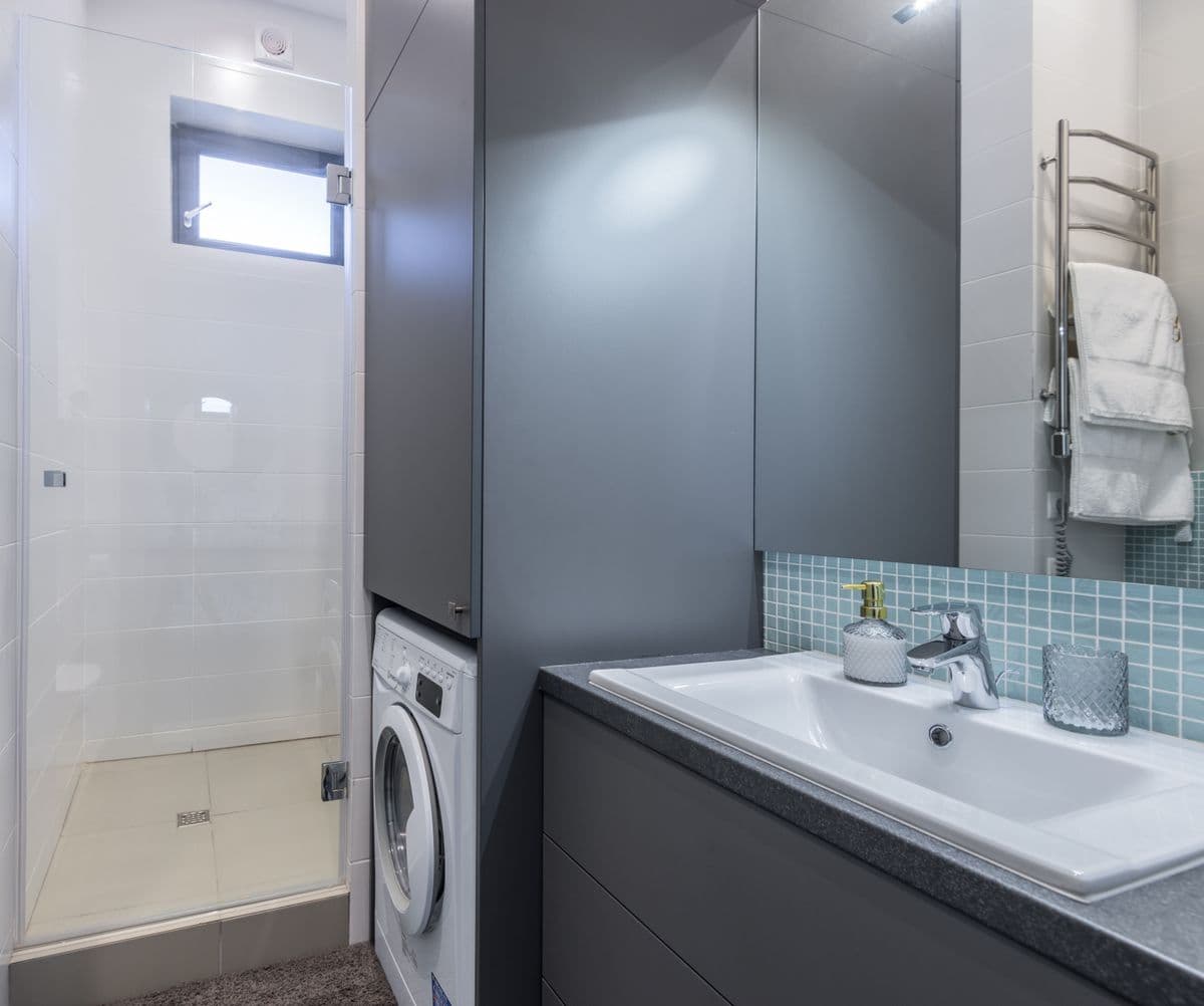 Renovated bathroom with a glass shower, floating vanity, and stacked laundry nook