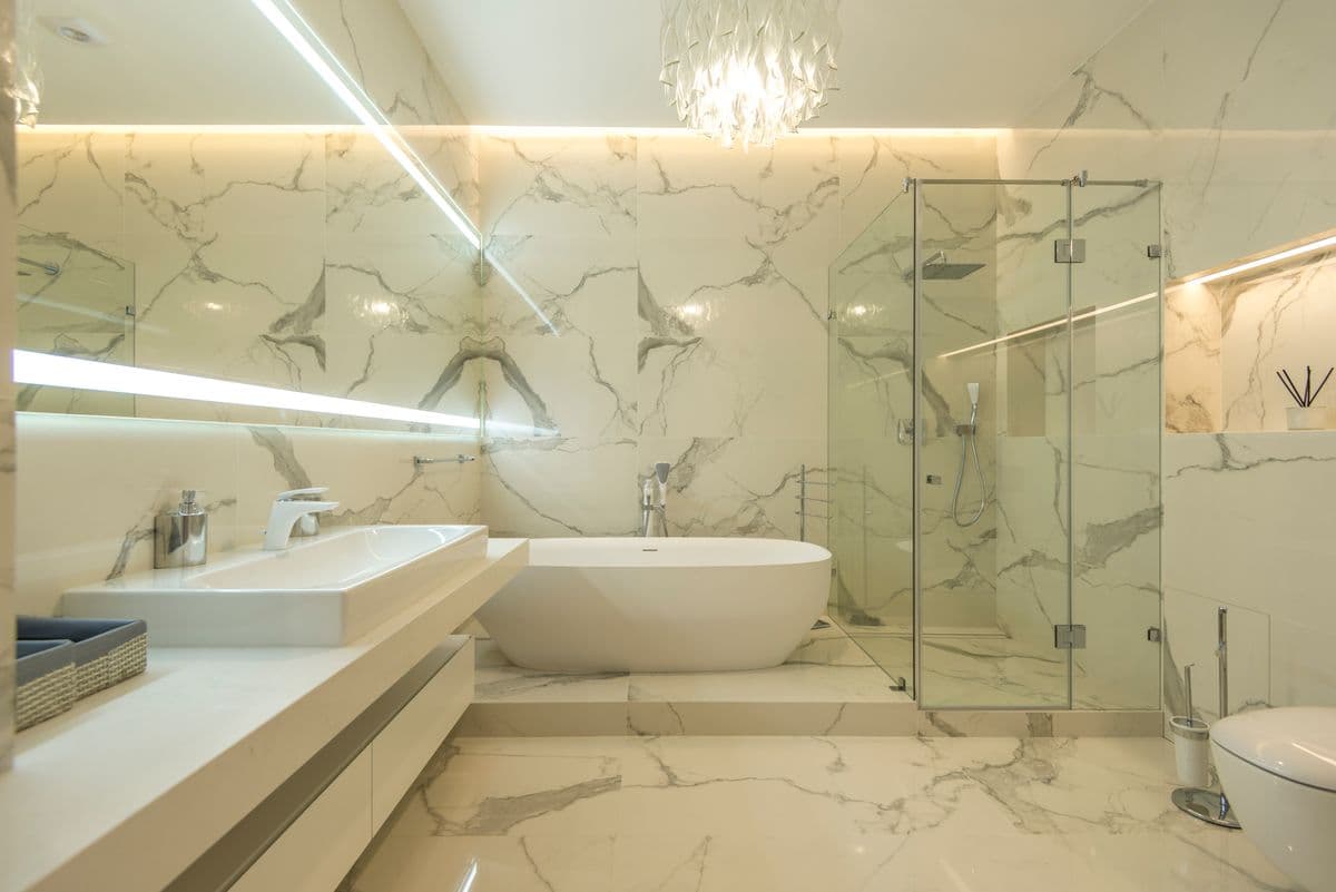 Full bathroom renovation featuring marble-look tile and a chrome fixture package