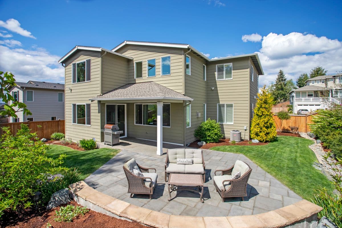 Backyard paver patio with a wicker seating set behind a two-story home