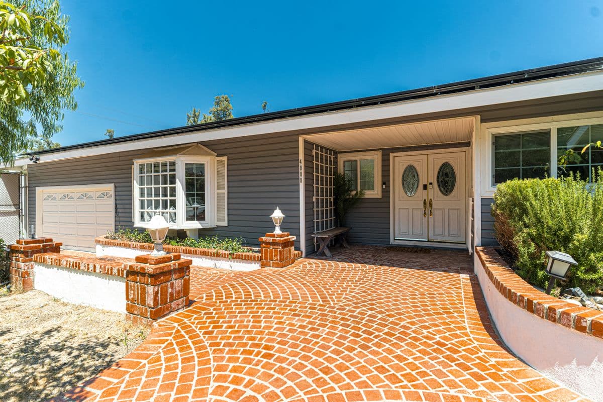 Ranch-style home exterior with a new brick paver driveway and entry walkway