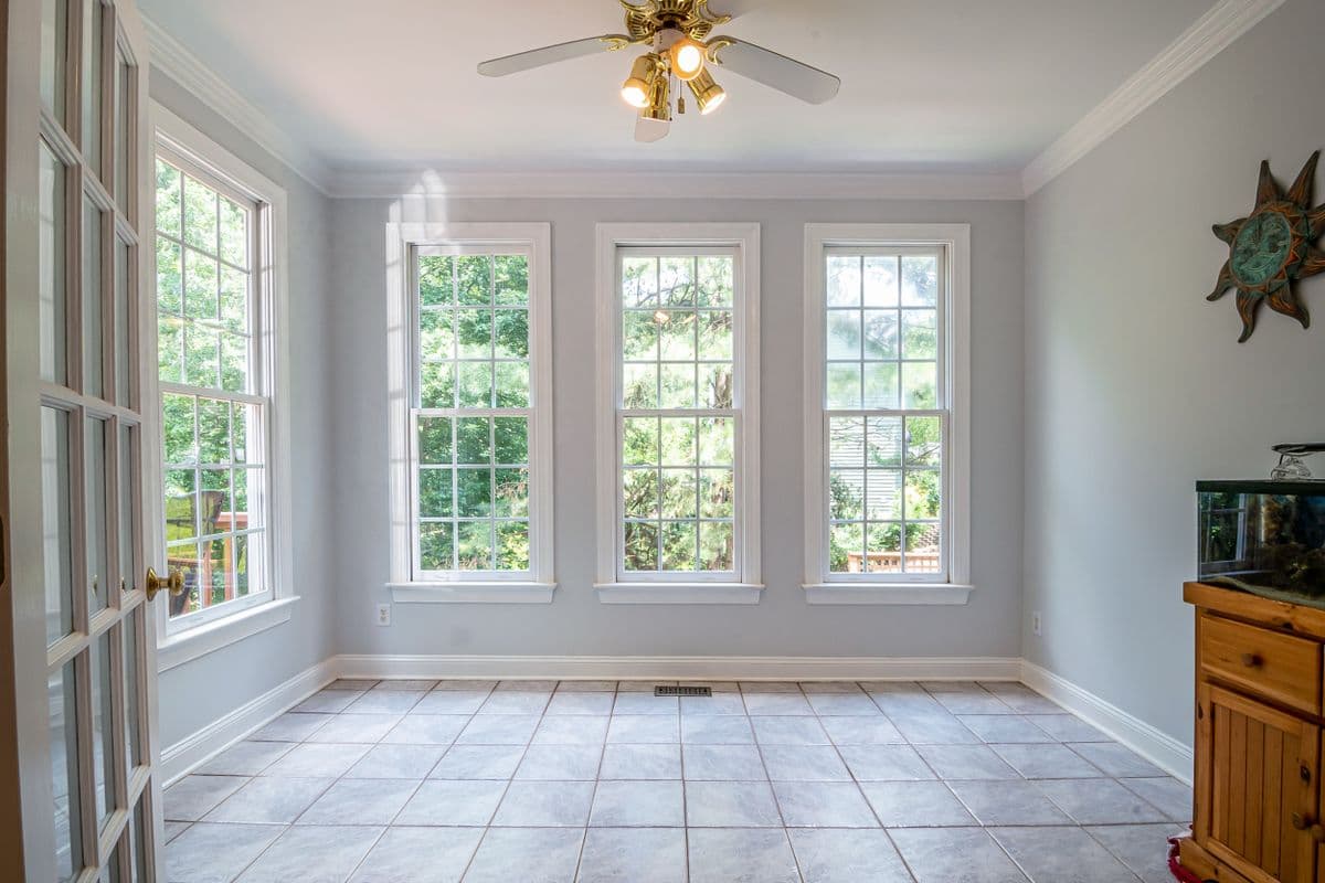 Tile flooring installed in a bright sunroom with a ceiling fan and garden view