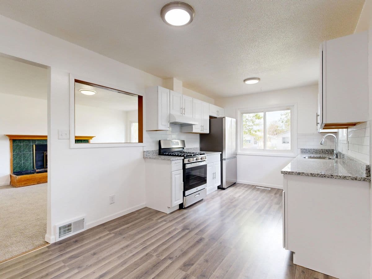 Bright white kitchen opening into a living room with new wood-look flooring