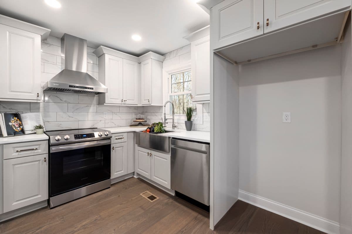 White shaker kitchen with a range hood and an open cabinet bay awaiting trim